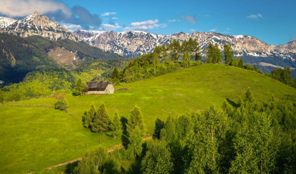 Sunlit alpine meadows, a wooden cabin and rocky mountain peaks in Romania